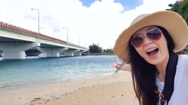 Asiática moderna chica gestos espectáculo en el mar y hacer un video en vivo en Naminoue Beach para compartir la maravillosa vista wuth sus amigos en las redes sociales
. - Metraje, vídeo