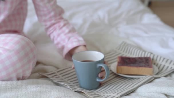 Young modern lady having her breakfast in her bed.She drank a cup of hot tea and toast with jam. She enjoys this wonderful brunch. - Video, Çekim