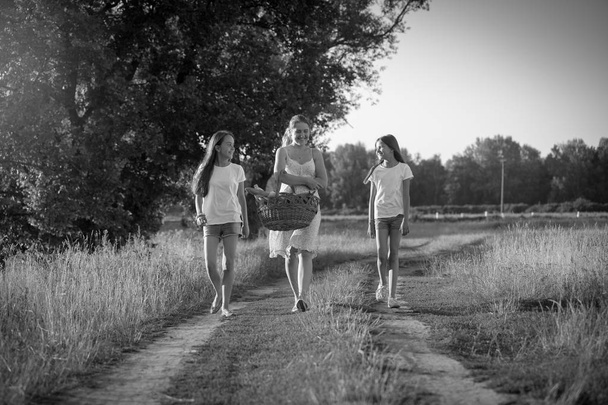 Черно-белое изображение двух девушек, идущих с матерью на пикник в поле
 - Фото, изображение