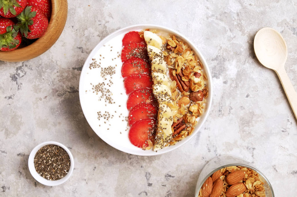 Wooden smoothie bowl, assorted ingredients on table. Healthy nutritious breakfast with vegan yogurt, raw fruits, nuts and cereals. - Φωτογραφία, εικόνα