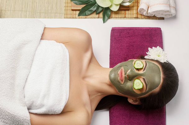 Woman with clay facial mask  and cucumbers on eyes in beauty spa - Photo, image