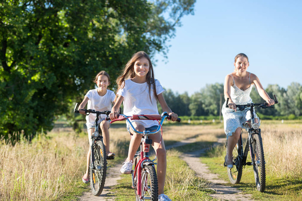Porträt von drei glücklichen Mädchen auf Fahrrädern im Feld bei sonnigem Tag - Foto, Bild