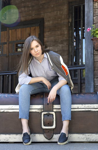 girl in jeans, shirt and sweatshirt sitting on a large chest aga - Foto, imagen