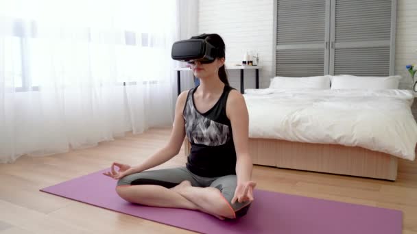 Asain woman wearing VR headset and sitting on the yoga mat. She puts her lotus fingers on her knees. - Záběry, video