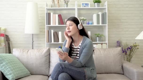 Asian woman enjoying sitting in the living room and swaying and singing the music during her pleasant Sunday afternoon. - Filmati, video