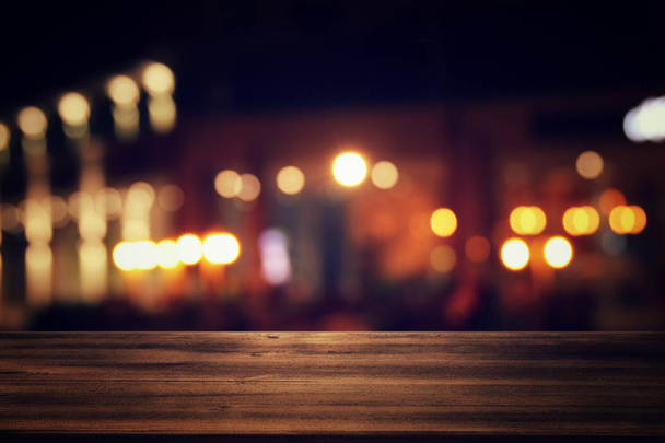 Image of wooden table in front of abstract blurred restaurant lights background. - Foto, immagini