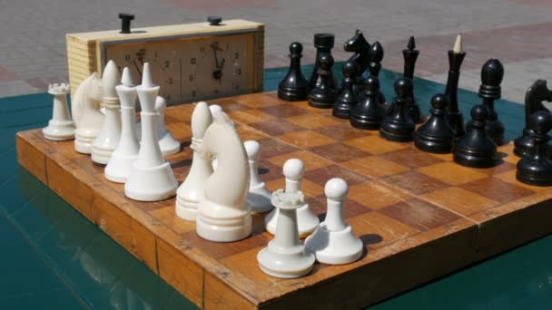 Musta ja valkoinen shakki seistä pöydällä, vieressä vuosikerta shakki kello kadulla
 - Materiaali, video
