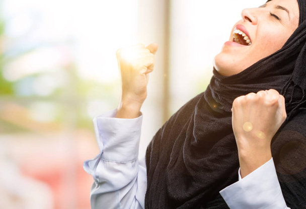 Mutlu ve heyecanlı kazanan jest ifade hijab giyen genç Arap kadın. Başarılı ve zafer, zafer kutluyor - Fotoğraf, Görsel