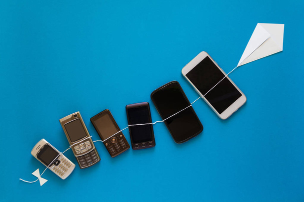 Technology evolution concept. Vintage and new phones flying on paper kite on blue sky.  - Foto, imagen