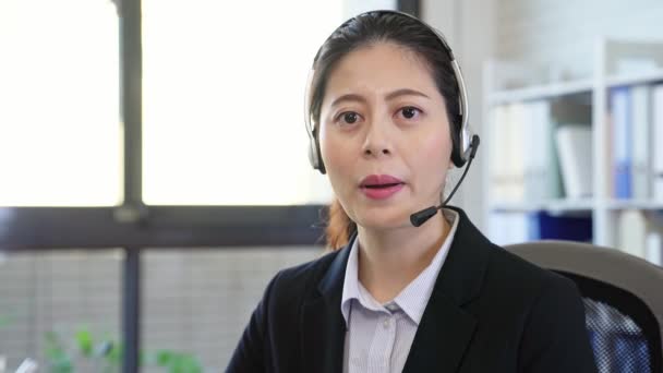 concepto de comunicación y tecnología de servicio en línea. sonriente asiático operador de línea de ayuda femenina con los auriculares sobre fondo de oficina
 - Metraje, vídeo