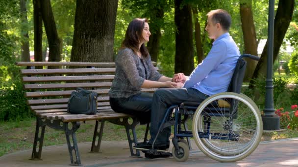 Mladý muž na vozíku mluvit se svou ženou v parku. Podpořit jeho zakázané manžel manželka. Zpomalený pohyb 4k - Záběry, video