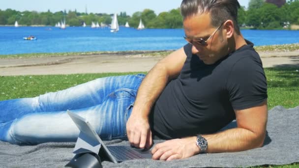 Um homem relaxa ao ar livre com bom tempo e surfa no laptop
 - Filmagem, Vídeo