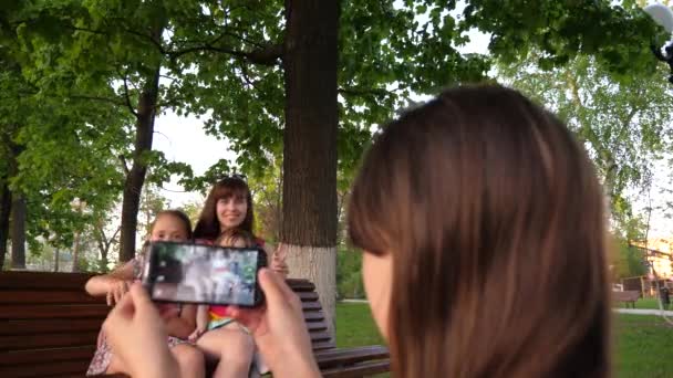 Jong meisje neemt foto's van haar moeder, zus en klein kind op telefoon. - Video