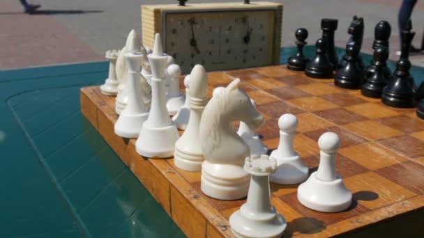 21 avril 2018 - Kamenskoye, Ukraine : Des échecs noirs et blancs se dressent sur l'échiquier, à côté d'une horloge d'échecs vintage dans la rue
 - Séquence, vidéo
