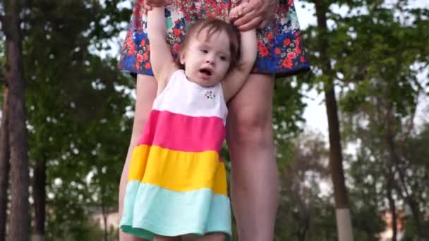 Mom teaches her little daughter to walk with her feet, holding her hands. - Materiał filmowy, wideo