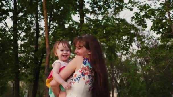 若い母親は笑って、彼女の腕の中で震えて小さな赤ちゃんと一緒に公園で遊ぶ. - 映像、動画