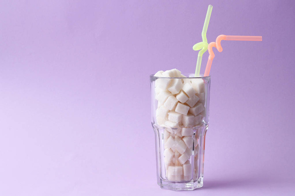 Un verre transparent rempli de sucre sur fond pastel avec de l'espace pour le texte. cubes de sucre. minimalisme, diabète, calories, boissons sucrées
.  - Photo, image