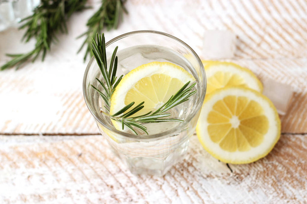 Wasser in einem Glas mit Zitrone und Rosmarin auf einem hölzernen Hintergrund. Kühlung und frische Getränke. - Foto, Bild
