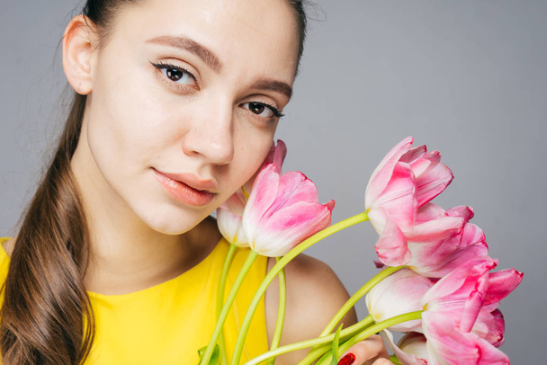 beautiful young girl model in yellow dress holds fragrant pink flowers, looks into camera and poses - Foto, Imagem