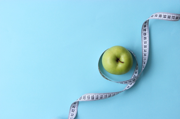 Apfel und Zentimeterband auf farbigem Hintergrund mit einem Platz zum Einfügen des Textes. Minimalismus, Draufsicht. Konzept Ernährung, gesunde Ernährung, schöner Körper, Sport. - Foto, Bild