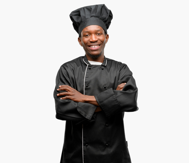 junge schwarze Köchin mit Kochmütze mit verschränkten Armen selbstbewusst und glücklich mit einem großen natürlichen Lächeln lachend - Foto, Bild