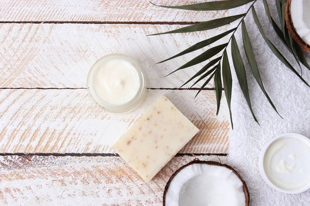 Cosmetische natuurlijke huidverzorgingsproducten van kokosnoot. Palm blad, kokosnoot en cosmetische crème op een houten achtergrond. minimalisme, de top. flatlay  - Foto, afbeelding