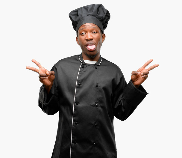 Fiatal fekete főzni rajta szakácssapka, lebukós látszó-on fényképezőgép találat tong, és így a győzelem ujjaival jel - Fotó, kép