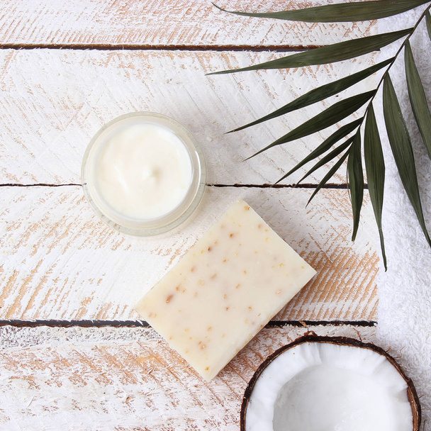 Cosmetic natural skin care products from coconut. palm leaf, coconut and cosmetic cream on a wooden background. minimalism, the top. flatlay  - Photo, Image