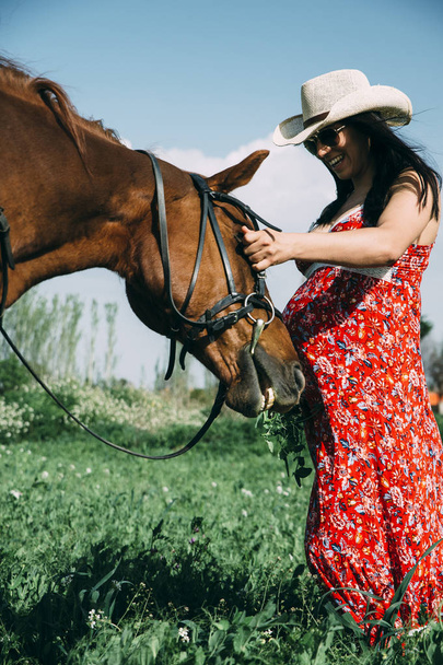 Raskaana oleva nainen hevosen kanssa vihreällä pellolla
 - Valokuva, kuva