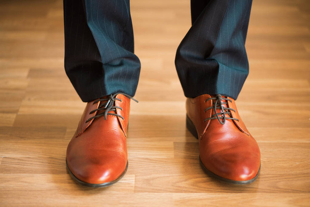 Man wearing shoes on wooden floor. Clothing concept, groom getting ready before ceremony. Body detail of businessman. - Фото, изображение