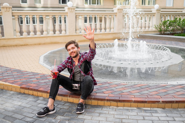 portrait de jeune homme barbu en chemise à carreaux boisson jus de plein air dans le centre-ville sur fond de fontaine
 - Photo, image