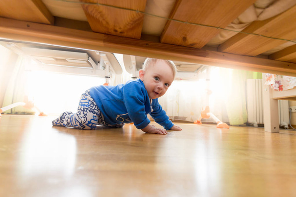 Δείτε από κάτω από το κρεβάτι του χαριτωμένο χαμογελαστό αγόρι toddler σέρνεται στο υπνοδωμάτιο - Φωτογραφία, εικόνα