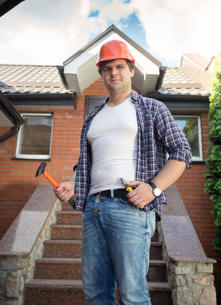 Портрет улыбающегося молодого строителя в каскаде, позирующего с инструментами в новом доме
 - Фото, изображение