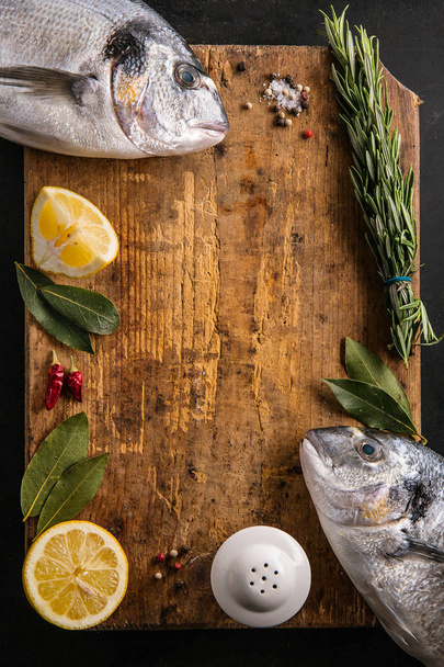 two dorado fish with lemon and rosemary at cutting board - Foto, Imagen