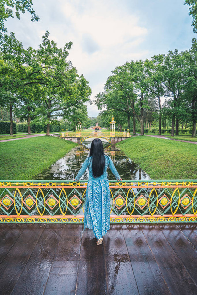 Młoda brunetka Kobieta w pięknej sukni, stojąc na mały mostek w Siele, Rosja w okresie letnim. Zielony las i rzeczka na tle. - Zdjęcie, obraz