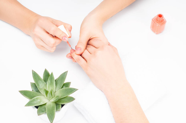 Manicure. Manicurist applies nail polish on female finger at salon - Fotó, kép