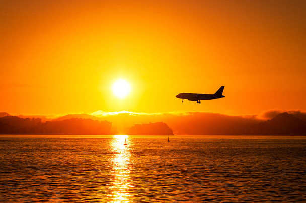 Flugzeug fliegt bei Sonnenuntergang tief über dem Wasser - Foto, Bild