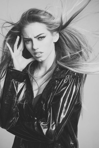 Lady sexy in slicker or raincoat suffers headache. Girl with long hair wears black cloak, grey background. Woman attractive on painful face touches temples. Headache concept - Foto, Bild