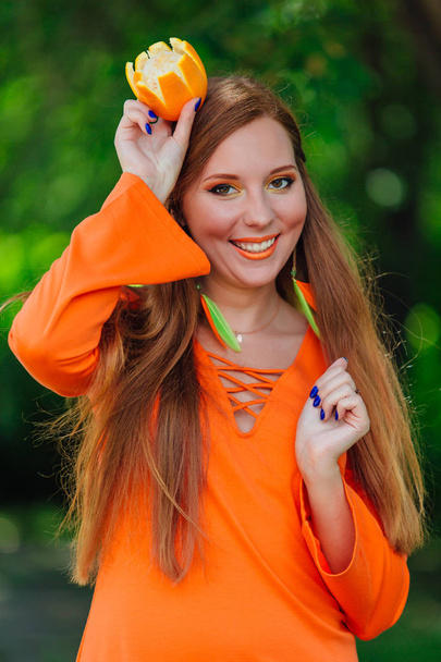 Retrato de bonita mujer pelirroja con jugosa naranja deliciosa como una corona en el parque verde de verano
. - Foto, Imagen