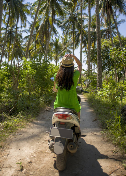 young happy tourist woman with hat riding scooter motorbike in tropical paradise jungle  with blue sky and palm trees exploring trip destination - Fotoğraf, Görsel
