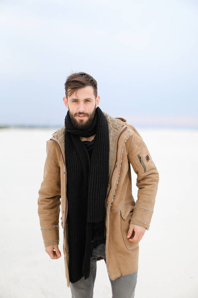 European young man with beard wearing coat and scarf standing in white snow background. - Foto, Imagen