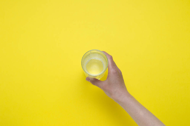 Female hand holding a glass of clean water on a yellow backgroun - Valokuva, kuva
