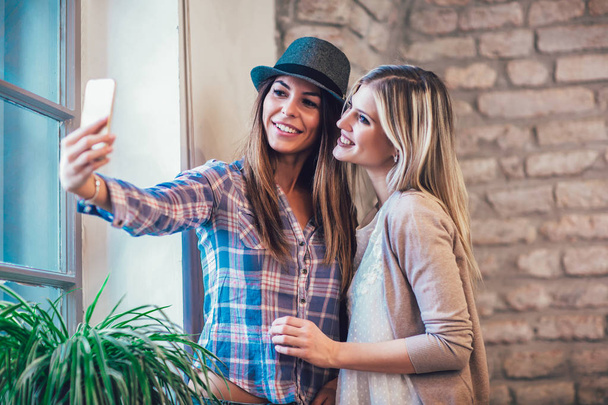 Портрет молодих усміхнених друзів-жінок, які використовують смартфон, роблять фото селфі
. - Фото, зображення