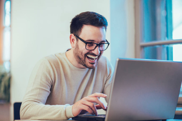 Jeune homme heureux, portant des lunettes et souriant, comme il travaille sur son ordinateur portable pour faire toutes ses affaires
 - Photo, image