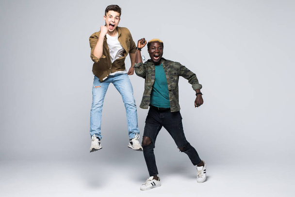 Портрет двух смешанных рас веселых молодых людей, прыгающих и празднующих изолированные на белом фоне
 - Фото, изображение