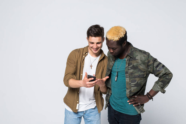 Jonge twee internationale vrienden telefoon geïsoleerd op een witte achtergrond gebruiken. Multiraciale vriendschap - Foto, afbeelding