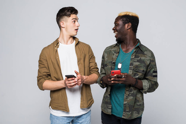 Two multiracial friends use their mobile phone isolated on white background. Phone addiction. - Photo, Image