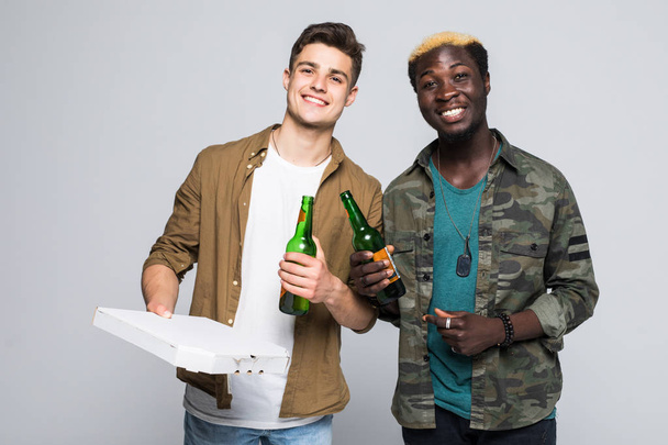 Muotokuva kahdesta onnellisesta sekarotuisesta nuoresta miehestä, jotka juovat olutta ja syövät pizzaa seisoessaan eristyksissä valkoisella pohjalla
 - Valokuva, kuva