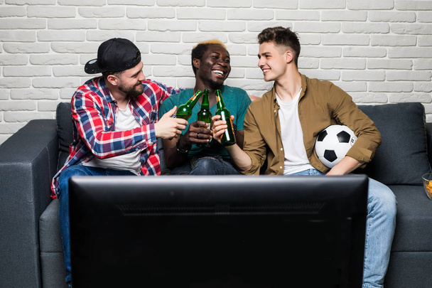 Happy cheerful men holding glass of beer cheers while watching tv - Fotó, kép