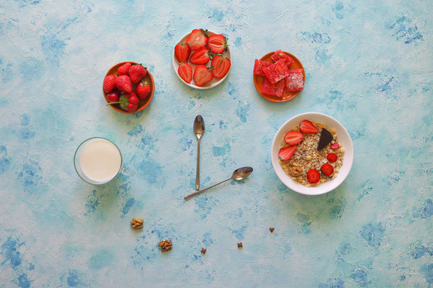 Φράουλα, μούσλι, γάλα και λουκούμι σε ένα τυρκουάζ τραπέζι. Ώρα για πρωινό. Κουτάλια Εμφάνιση ώρας. - Φωτογραφία, εικόνα